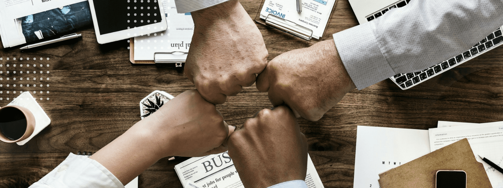 A group of people seated at a table, holding hands and surrounded by papers, symbolizing unity and collaboration